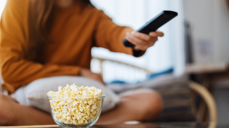 Sfeerfoto waarop een persoon een remote vasthoudt om televisie te kijken.
