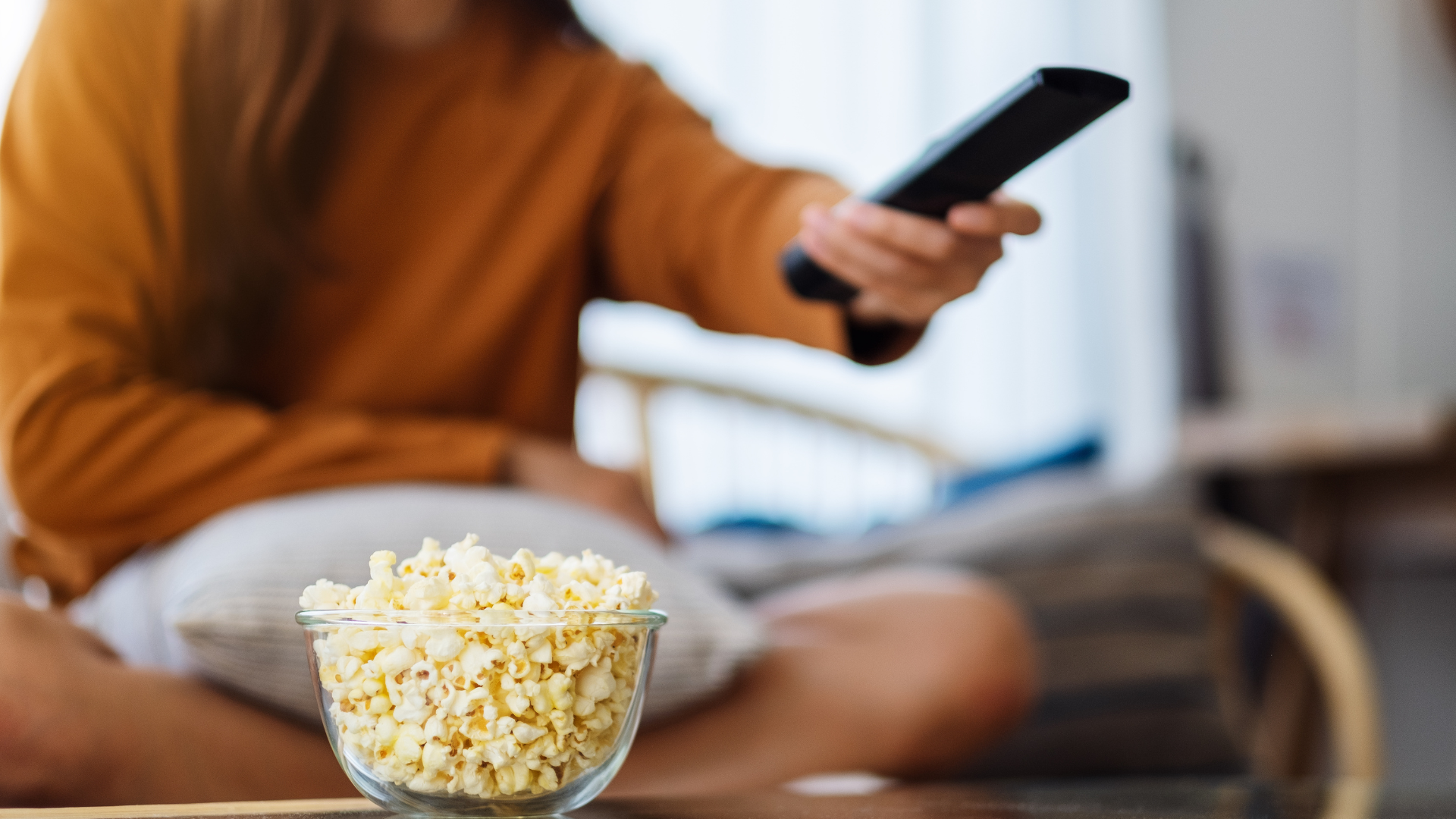Sfeerfoto waarop een persoon een remote vasthoudt om televisie te kijken.